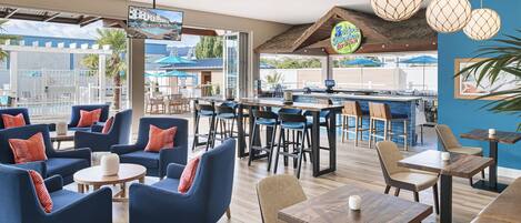 A modern bar area with blue and brown seating, a pool view, and hanging spherical light fixtures.