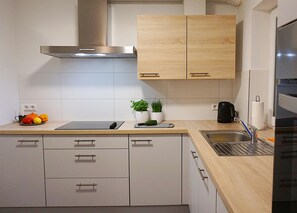 A modern kitchen with wooden cabinets, a stainless steel range hood, a sink, and a countertop with a cutting board and potted plants. - Klötzle Blei - cozy basement vacation apartment with terrace for 2 people (Blaubeuren)
