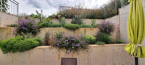A tiered garden with various plants and flowers, a concrete wall, and a green umbrella.