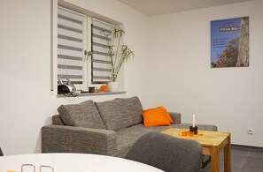 A living room with a grey sofa, a small table with a candle, and a window with blinds. - Klötzle Blei - cozy basement vacation apartment with terrace for 2 people (Blaubeuren)