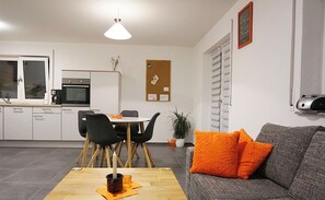 A modern living room with a dining area, a kitchen, and a grey sofa with orange cushions. - Klötzle Blei - cozy basement vacation apartment with terrace for 2 people (Blaubeuren)
