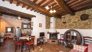 Un interior rústico con pared de piedra, vigas de madera, chimenea, zona de comedor y un rincón de estar acogedor.