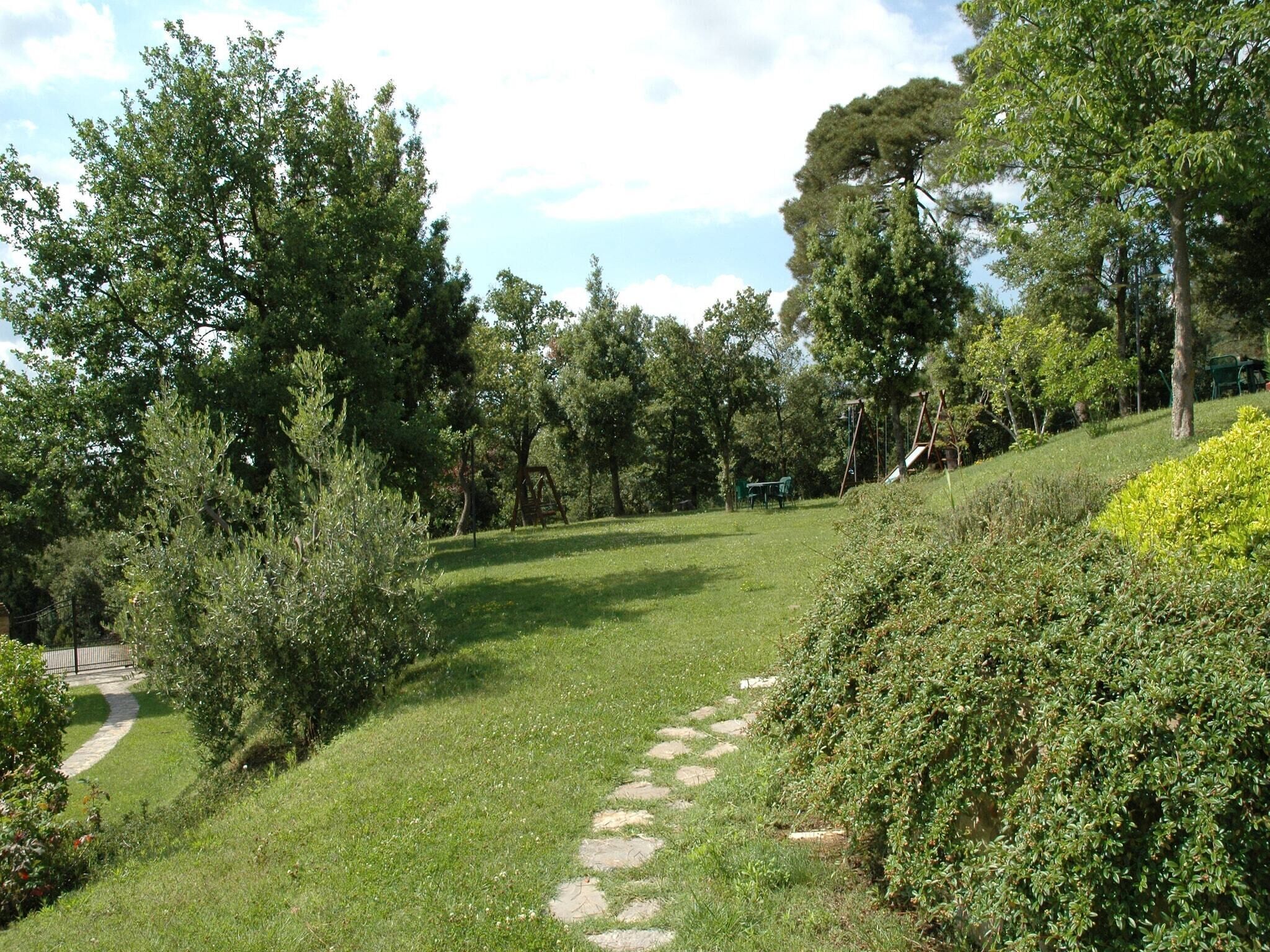 A grassy pathway with trees and a swing set in a park.