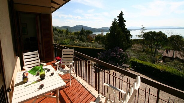 A balcony with a table and chairs, overlooking a scenic landscape with mountains and a body of water.