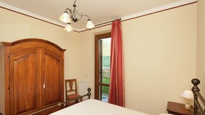 Een slaapkamer met een grote houten garderobe, een bed met wit beddengoed, een nachtkastje met een lamp en een raam met rode gordijnen.