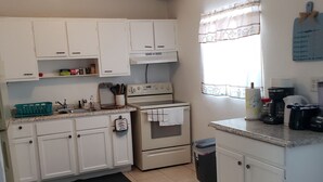 A kitchen with white cabinets, a stove, and a sink. There is a bowl of fruit on the table. -   5min drive to Universal studio (Orlando)