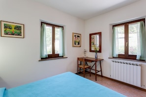 Une pièce comprenant un lit, un bureau, deux fenêtres avec des rideaux, un radiateur et deux tableaux encadrés accrochés au mur.