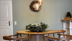 Un comedor con una mesa redonda de madera, seis sillas de madera con cojines grises y tres lámparas colgantes.