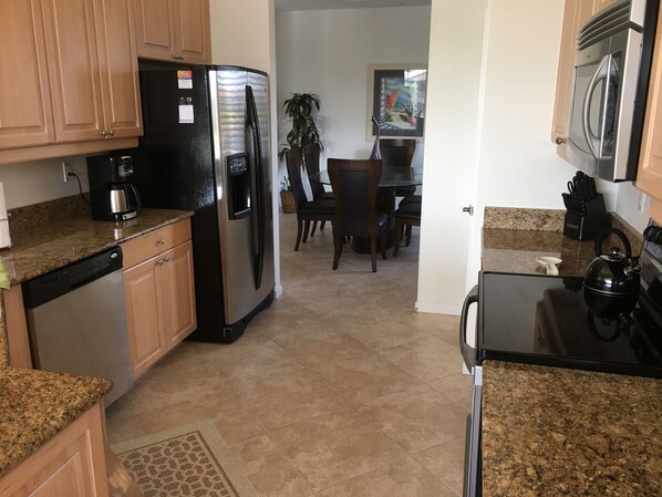A kitchen with granite countertops, stainless steel appliances, wooden cabinets, and a dining area with a table and chairs.