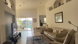 Ein geräumiges Wohnzimmer mit einer großen Couch, einem Couchtisch und einem Fernseher. Es gibt einen Balkon mit Blick ins Freie.