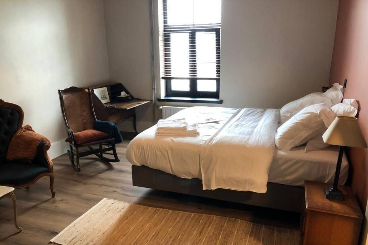A bedroom with a bed, a chair, a desk, and a window.