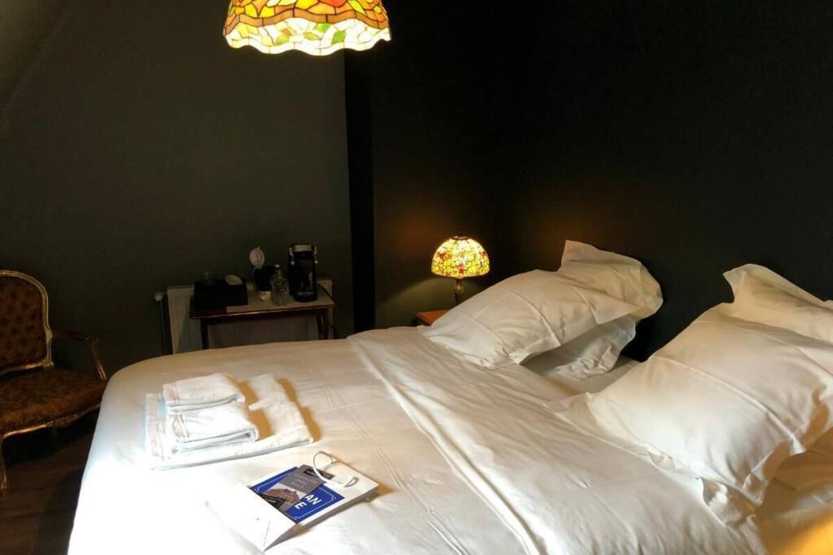 A hotel room with a large bed, two bedside tables, a chair, and a stained glass lamp.
