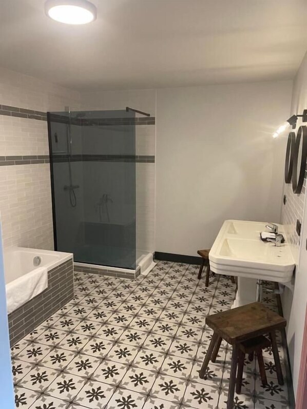 A bathroom with a glass-enclosed shower, a white sink, and a small wooden stool.