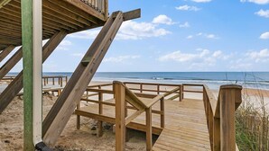 Un muelle de madera bordeando la playa que lleva al océano, con vista despejada al mar y al cielo.