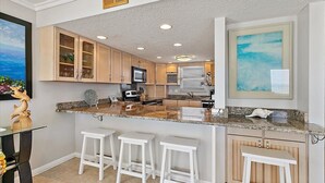 Una cocina moderna con encimeras de granito, taburetes de bar blancos y armarios de madera.