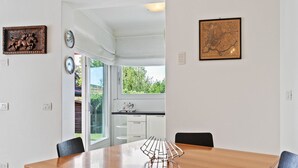 Un coin repas avec une table en bois, des chaises noires et un élément décoratif en métal. On y trouve des meubles blancs et une fenêtre donnant sur un paysage verdoyant.