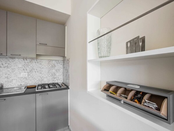 A modern kitchen with grey cabinets, a gas stove, and a built-in storage unit with kitchen utensils.