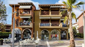 Un hotel de varios pisos con mesas al aire libre, balcones y una palmera.