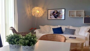 Una sala moderna con un sofá blanco, una mesa de centro redonda, sillas de mimbre y un accesorio de iluminación decorativo.