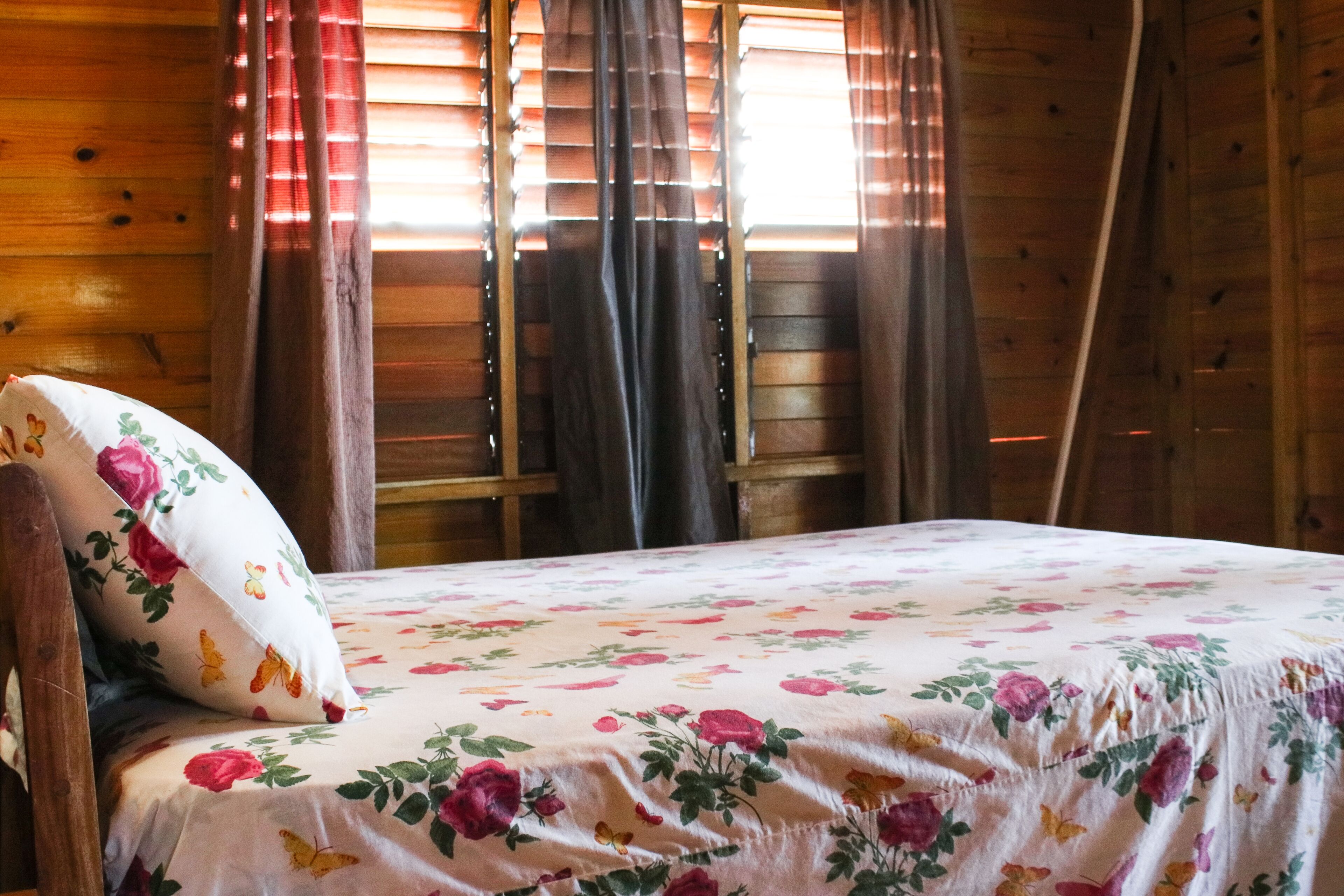 Una camera da albergo in legno con un letto, biancheria da letto floreale e tende.