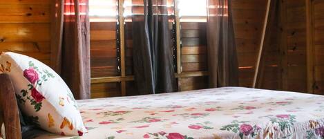 Una camera da albergo in legno con un letto, biancheria da letto floreale e tende.