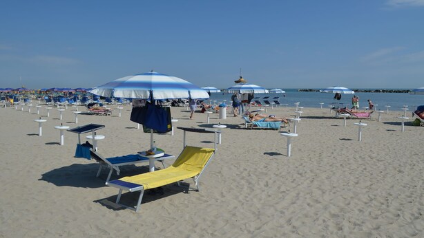 Una playa con múltiples tumbonas y sombrillas, algunas ocupadas y otras vacías.