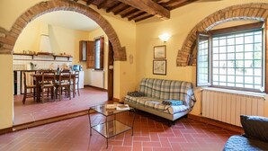 Una sala de estar con un sofá a cuadros, una mesa de centro de vidrio y un comedor con sillas y mesa de madera.