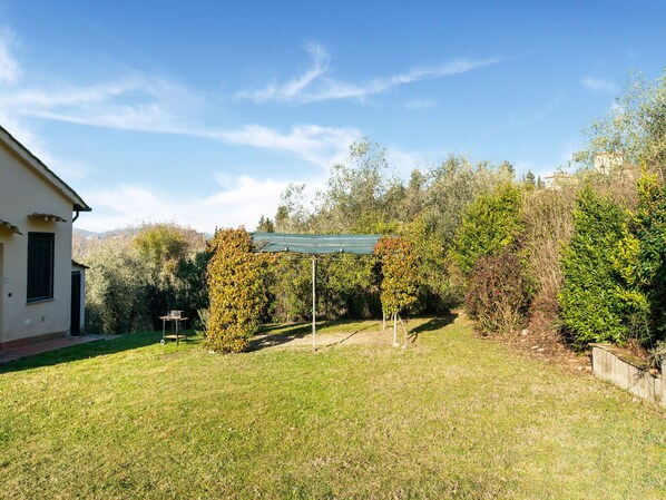 A house with a covered patio area, surrounded by a grassy yard and various trees.