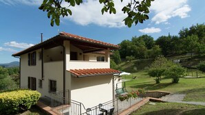 A two-story house with a tiled roof, a balcony, and a garden with potted plants.