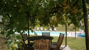 A covered outdoor seating area with a pool in the background.