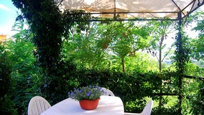 Un patio exterior con una mesa y sillas blancas, rodeado de abundante vegetación y un dosel blanco.