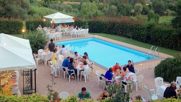 Zona de piscina al aire libre con mesas y sillas, rodeada de follaje.