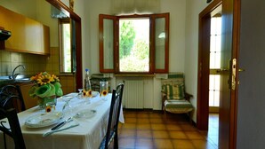 Un comedor con una mesa preparada para cuatro personas, sillas, una ventana que ofrece vistas a zonas verdes y un radiador.