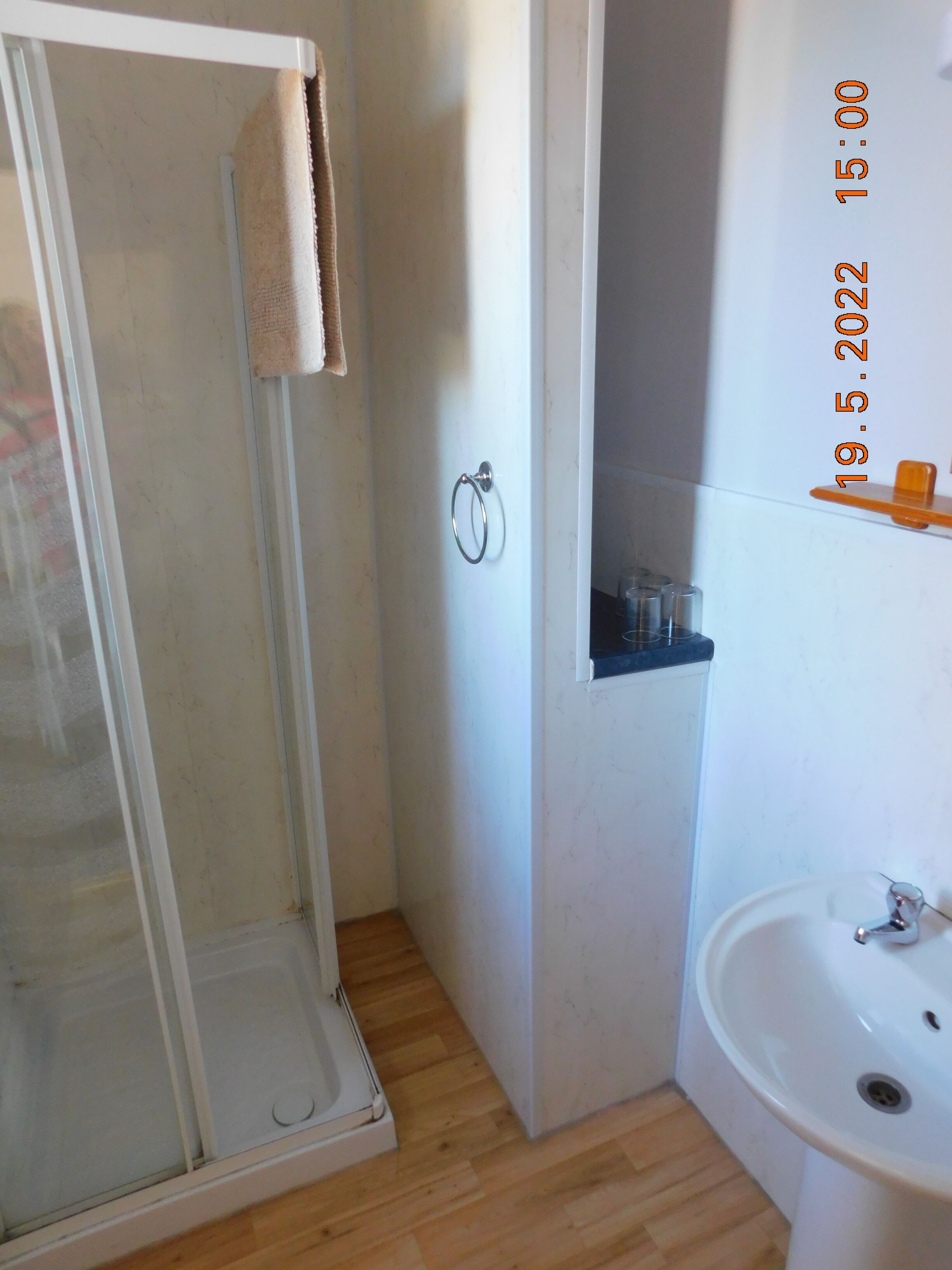 A bathroom with a glass shower enclosure, a white sink, and a shelf with toiletries.