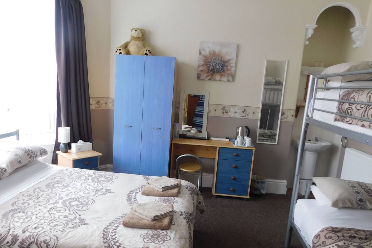 A hotel room with a bed, a desk, a wardrobe, a mirror, and a bunk bed.