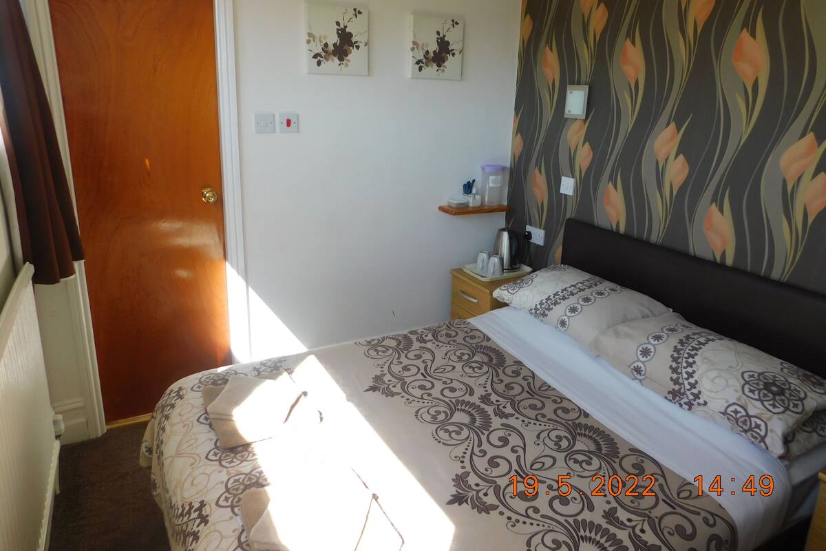 A bedroom with a bed, a nightstand, a shelf with toiletries, and a door.