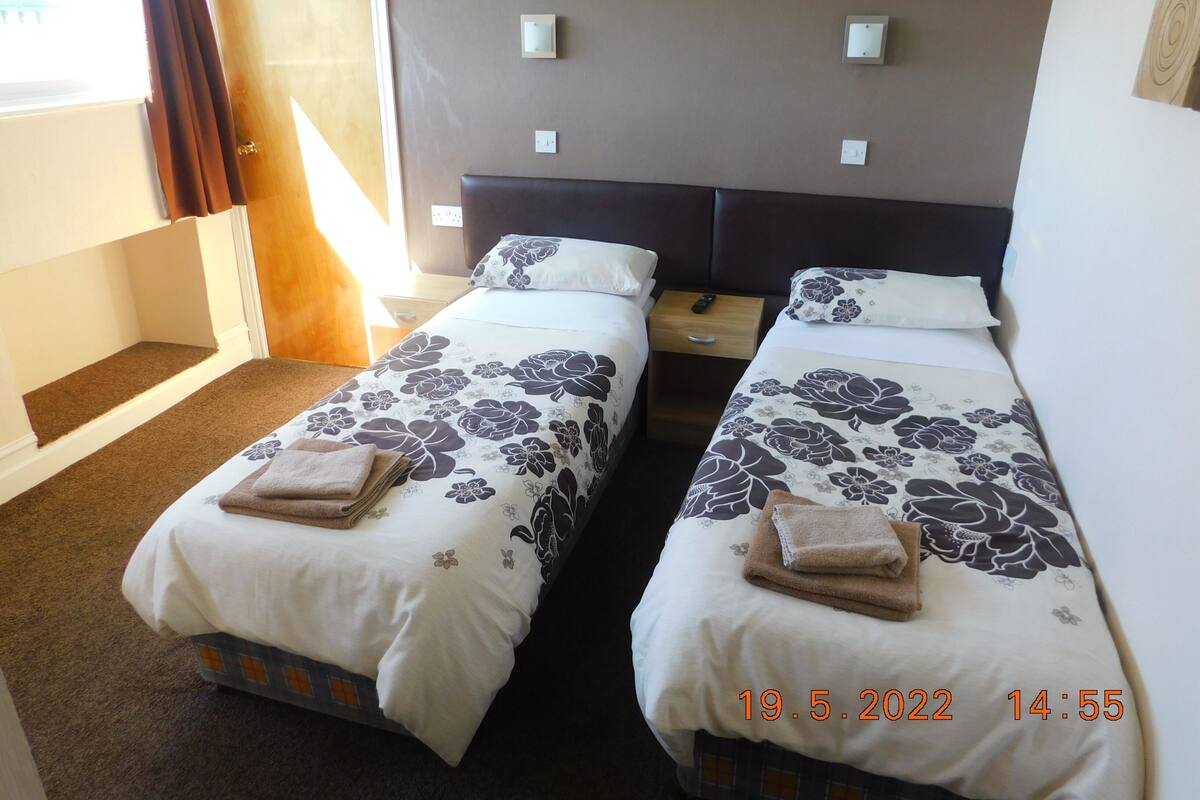 A hotel room with two beds, each with floral bedding and towels, a wooden nightstand, and a door leading outside.