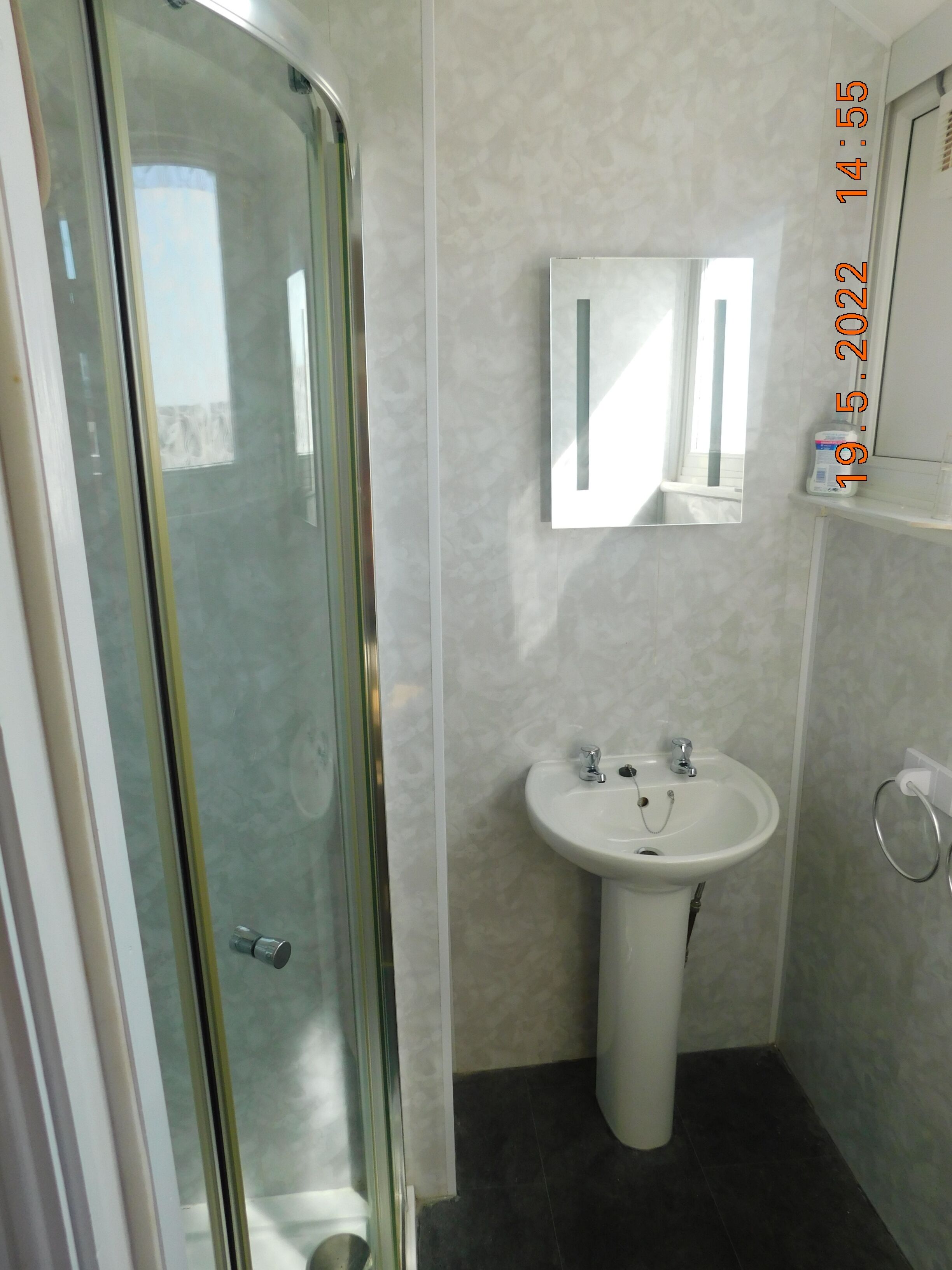 A bathroom with a glass shower enclosure, a pedestal sink, and a mirror above it.