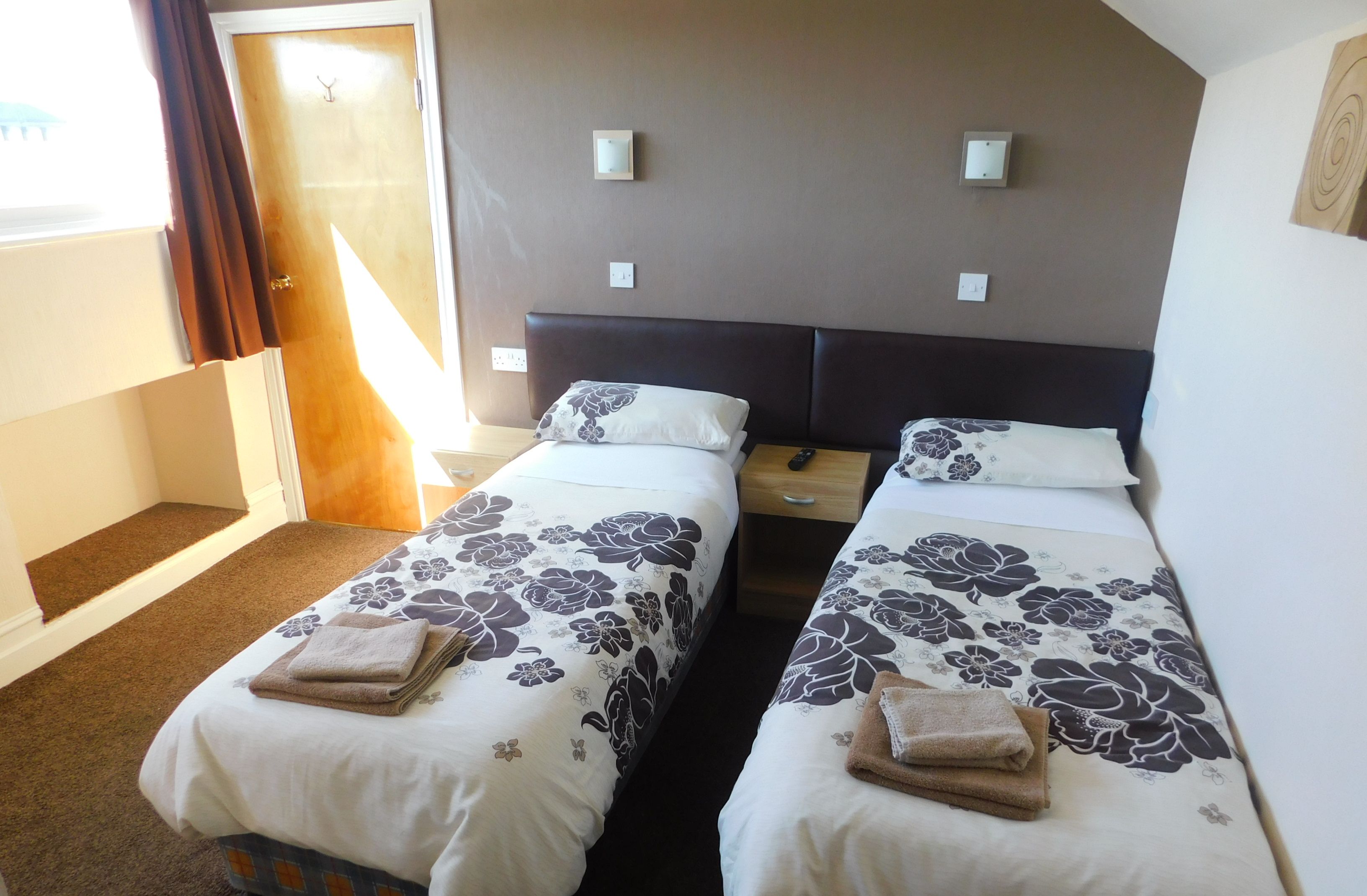 Ein Hotelzimmer mit zwei Betten, jeweils mit floralem Bettzeug und Handtüchern, einem hölzernen Nachttisch und einer Tür, die nach draußen führt.