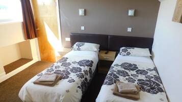 Ein Hotelzimmer mit zwei Betten, jeweils mit floralem Bettzeug und Handtüchern, einem hölzernen Nachttisch und einer Tür, die nach draußen führt.