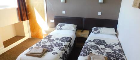 Habitación de hotel con dos camas, cada una con ropa de cama y toallas estampadas con motivos florales, una mesita de noche de madera y una puerta que da al exterior.