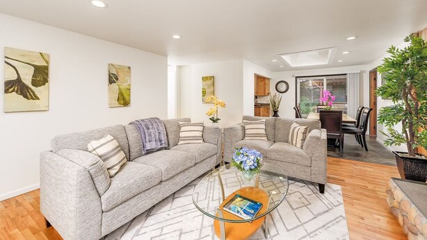 Ein modernes Wohnzimmer mit zwei grauen Sofas, einem Glastisch und einem Essbereich im Hintergrund.
