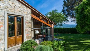 A stone building with a wooden door and large windows, surrounded by a well-maintained garden and a view of mountains. - Belvilla by OYO Gallorimpi (Dicomano)