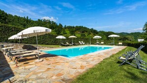 A swimming pool with lounge chairs and umbrellas, surrounded by stone tiles and greenery. - Belvilla by OYO Gallorimpi (Dicomano)