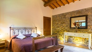A bedroom with a bed, a bench, a nightstand, a dresser, a stone wall, and a wooden ceiling. - Belvilla by OYO Gallorimpi (Dicomano)