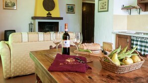 A cozy living room with a sofa, a wooden table with a bottle of wine, glasses, a basket of fruit, and a fireplace.