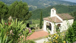 A white church with a bell tower, surrounded by lush greenery and hills in the background.