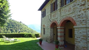A stone building with arched doorways and a paved walkway leading to a grassy area with outdoor seating.