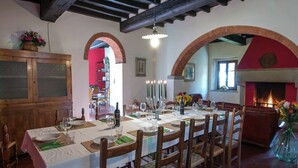 A dining area with a long table set for a meal, wooden chairs, and a brick fireplace.