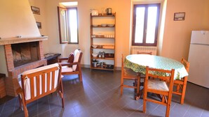 Una cocina acogedora con chimenea de ladrillo, sillas de madera, una mesa de comedor con mantel floral y un refrigerador blanco.